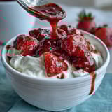 Strawberry compote drizzled over creamy Greek yogurt with fresh mint garnish, a light and refreshing dessert.  