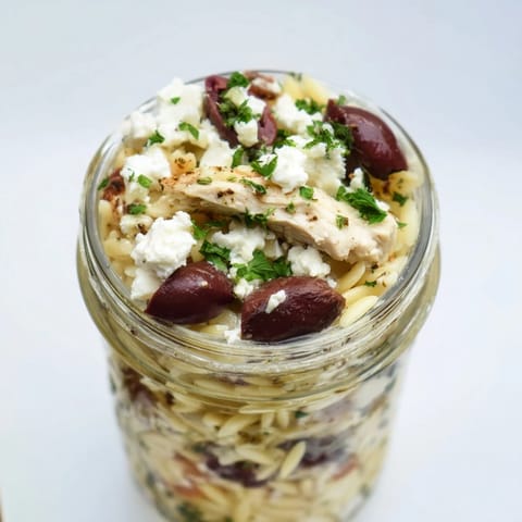 Layered Greek Pasta Chicken Salad Jars with orzo, grilled chicken, feta, and olives, showcasing colorful Mediterranean veggies for a fresh meal prep lunch.