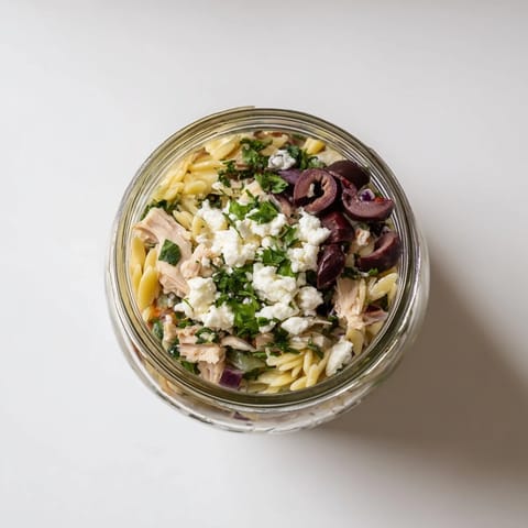 Bright jar of Greek Pasta Chicken Salad with cherry tomatoes, cucumbers, and crumbled feta, layered for grab-and-go ease in busy U.S. kitchens.