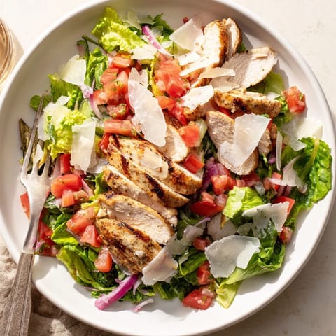 A close-up of Bruschetta Chicken Salad on a white plate, featuring juicy grilled chicken slices, a vibrant tomato-basil topping, and fresh mixed greens.