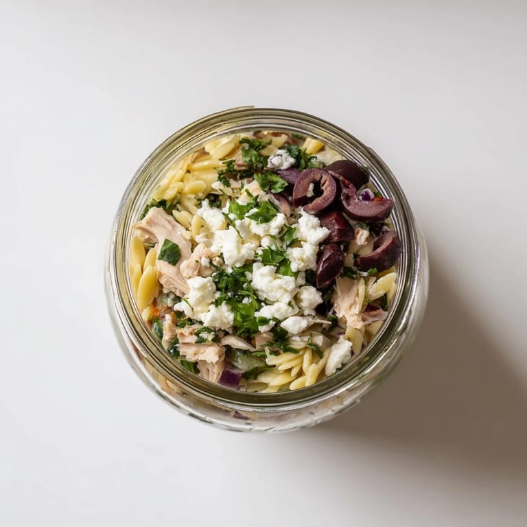 Bright jar of Greek Pasta Chicken Salad with cherry tomatoes, cucumbers, and crumbled feta, layered for grab-and-go ease in busy U.S. kitchens.