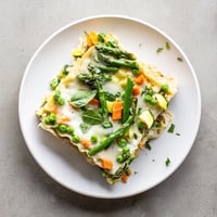 Spring Veggie Alfredo Lasagna features golden, bubbling cheese atop layers of creamy Alfredo, tender spring vegetables, and no-boil noodles.